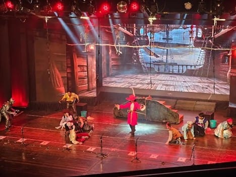 Stage performance at Balgandharva Rangmandir featuring dancers and actors in costume, with a ship-themed backdrop and theatrical lighting